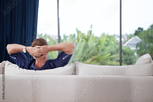 portrait of young man with hands behind his head is relaxing on couch photo