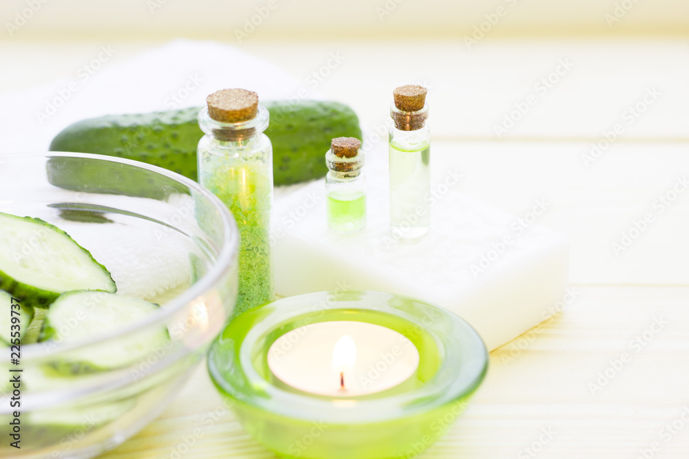 Cucumber home spa and hair care concept. Sliced cucumber, bottles of oil, jar of mask, bathroom towel. White board background Cucumber home spa and hair care concept. Sliced cucumber, bottles of oil, jar of mask, bathroom towel. White board background