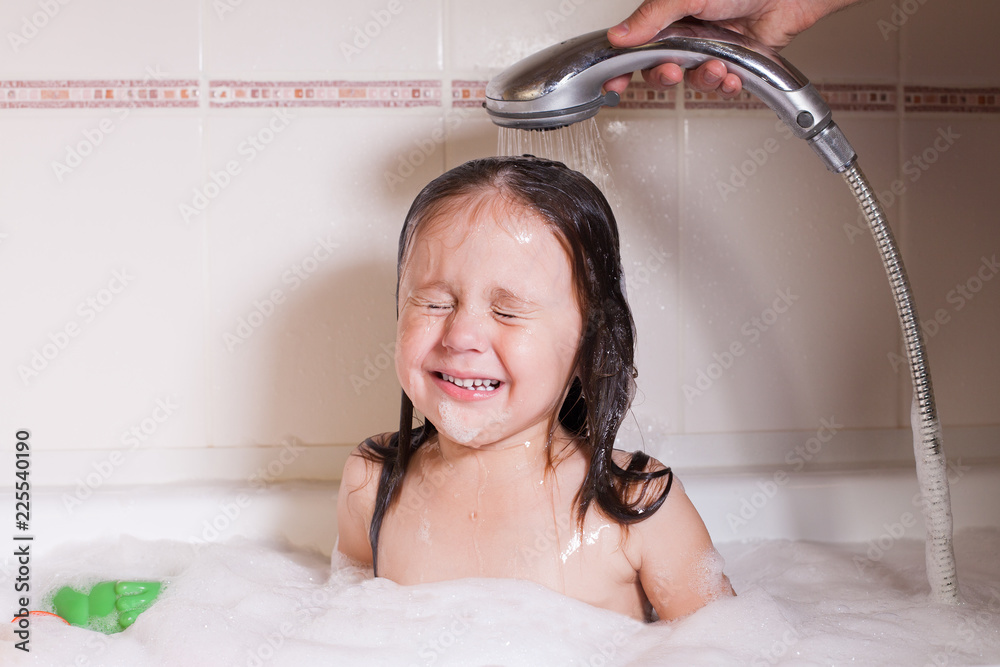 The little girl is crying in the bathroom, afraid to take a bath Stock