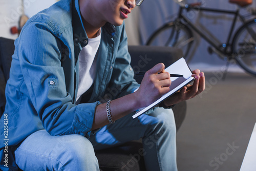 cropped shot of young man sitting on couch and writing in notebook
