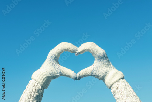 Female hands in the winter knitted gloves in the shape of a heart on the blue sky background. Concept