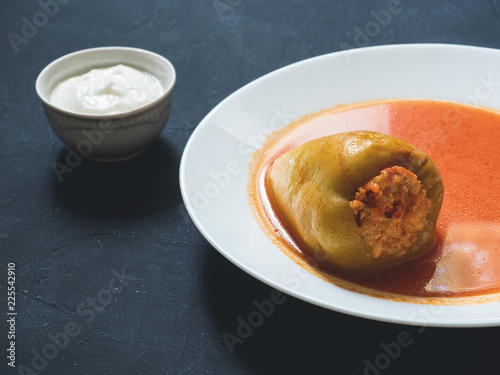 Stuffed pepper in a white plate with sour cream on a black background