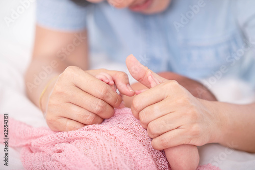 Selected focus on mother hands holds little baby covered by pink blanket in the bed.
