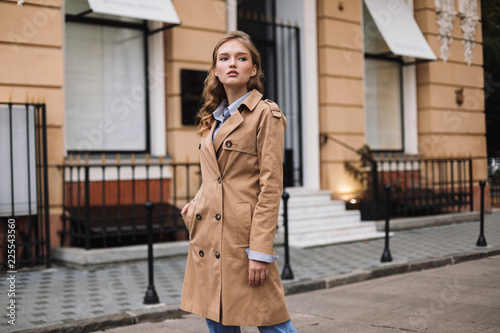 Foto Pretty thoughtful girl in trench coat dreamily looking aside while walking aroun