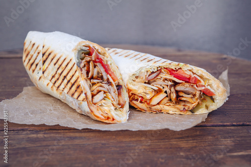 Shawarma sandwich gyro- fresh roll of thin lavash (pita bread) filled with grilled meat, mushrooms, cheese, cabbage, carrots, sauce, green. Traditional Eastern snack. On a wooden background