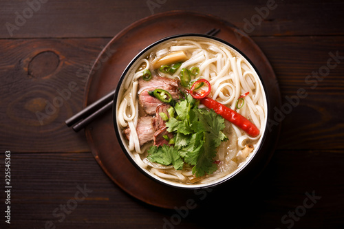 Vietnamese traditional soup Pho Bo with beef and fresh coriander on dark wooden background photo
