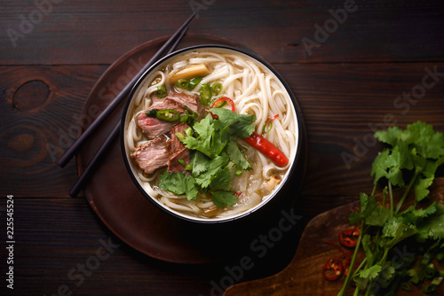 Vietnamese traditional soup Pho Bo with beef and fresh coriander on dark wooden background