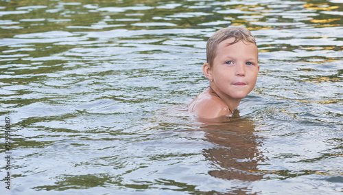 Portrait of happy fun little Caucasian boy swimming in the sea or lake. © cameravit