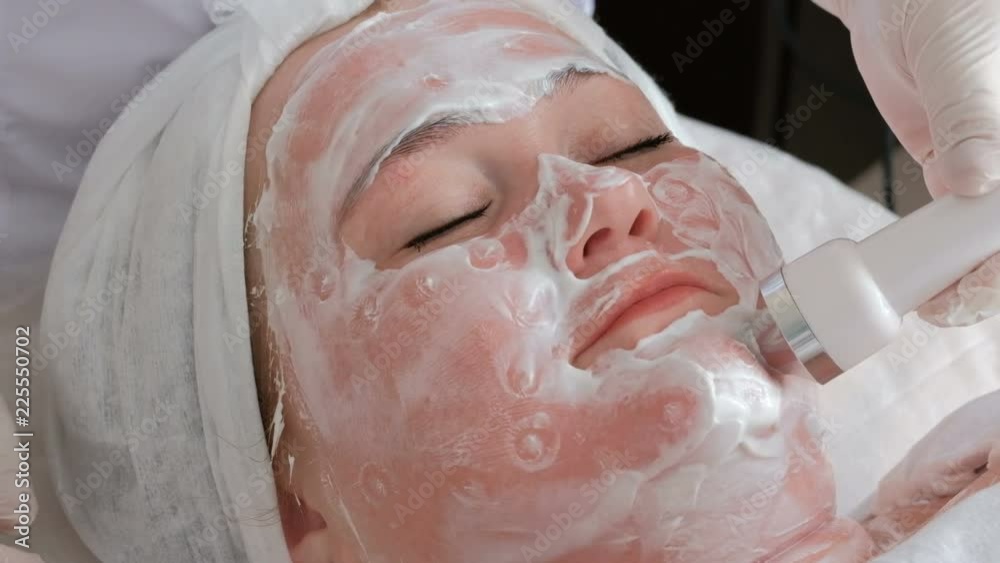 Physiotherapy procedure in the beauty salon. A woman undergoes phonophoresis of skin lifting. Beautician put points on the face with the help of a white handle of the ultrasonic massage apparatus. Physiotherapy procedure in the beauty salon. A woman undergoes phonophoresis of skin lifting. Beautician put points on the face with the help of a white handle of the ultrasonic massage apparatus.