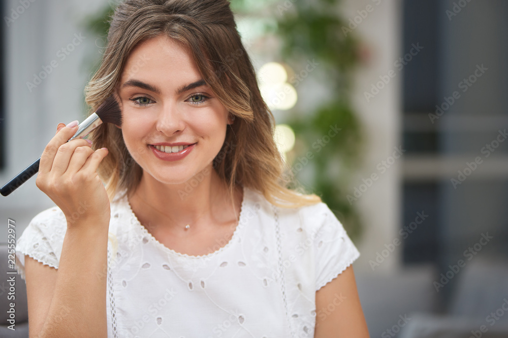 Portrait of charming girl fixing makeup with powder in salon Portrait of charming girl fixing makeup with powder in salon