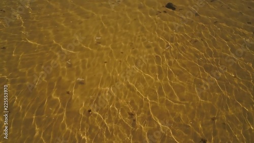 AERIAL PANNING UP. People walking along spit with mountainous mainland behind them.