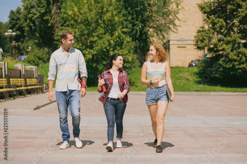 Three students walking in the park. Happy teens having conversation.