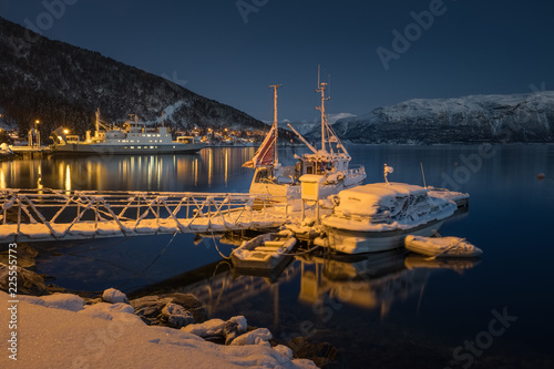 Winter landscape of a Norwegian village in winter with fishing boats at the forground. Moon over the fjord in Norway.