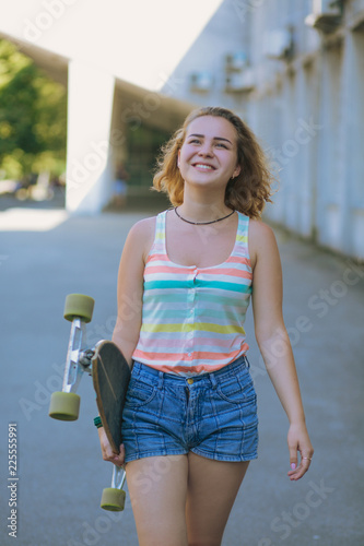 Pretty student with a skatebord in her hands. Smiling girl is about to ride a skateboard, which she holds in her hands. photo