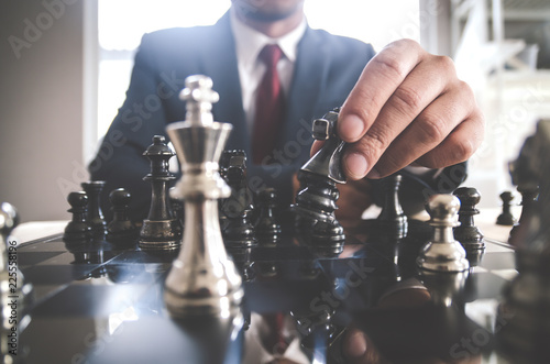 Retro style image of a businessman with clasped hands planning strategy with chess figures on an old wooden table.