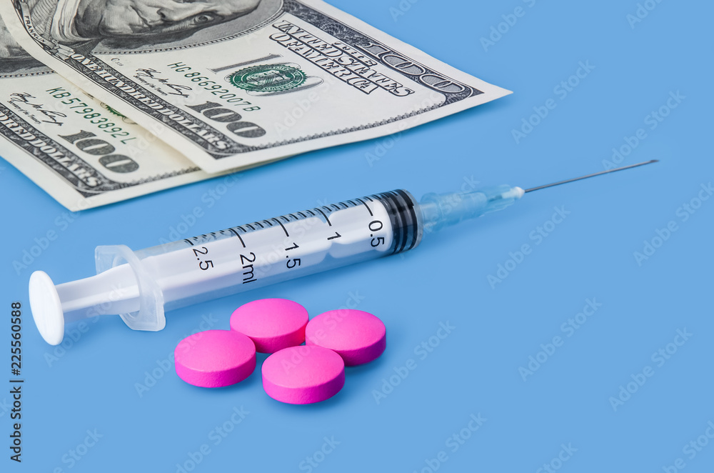 A syringe with a needle, pills and bills of one hundred dollars on a light blue background. A syringe with a needle, pills and bills of one hundred dollars on a light blue background.