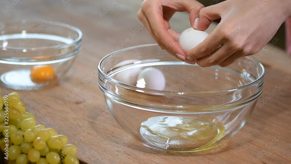 Woman hands breaking an egg to separate egg white and yolks and egg shells at the background. Woman hands breaking an egg to separate egg white and yolks and egg shells at the background.