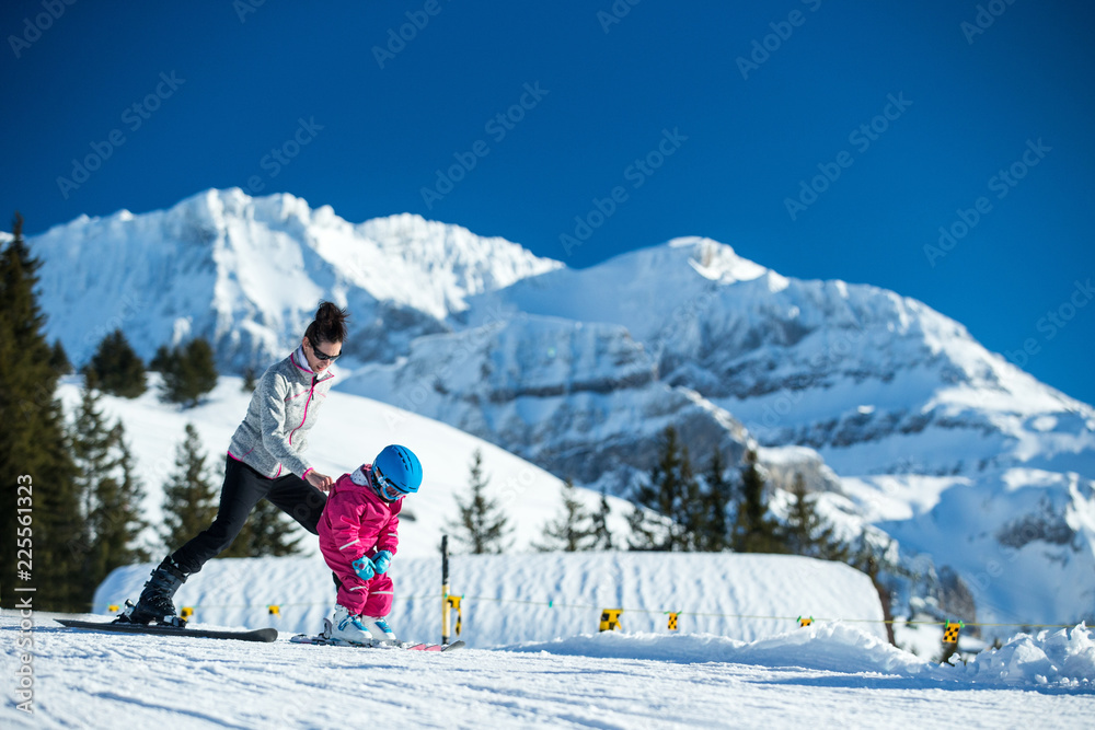 Mother and little child skiing in Alps mountains. Active mom and toddler kid with safety helmet, goggles and poles. Ski lesson for young children. Winter sport for family. Little skier, swiss Alps