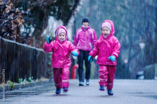 Girls are having fun in water on street in cold autumn day, girls splashing water in rain, happy and cheerful girls enjoying cold weather, kids in pink rain coats and rubber boots