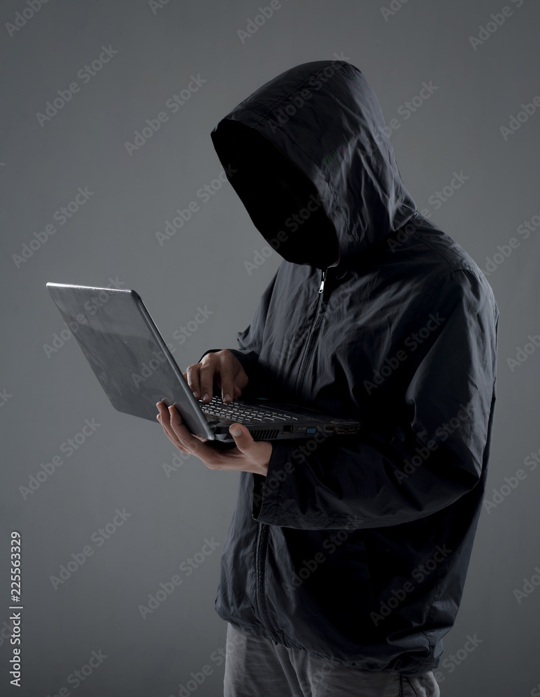 Hacker with hidden face in a hoodie using a laptop Hacker with hidden face in a hoodie using a laptop