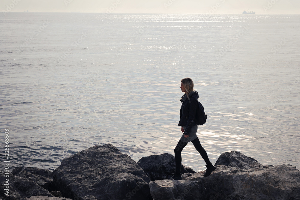 Young woman traveller walking on stone sea coast. Follow your dream concept Young woman traveller walking on stone sea coast. Follow your dream concept