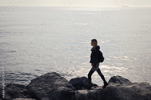 Young woman traveller walking on stone sea coast. Follow your dream concept