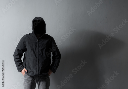 Mysterious man with hidden face in a hoodie against gray wall