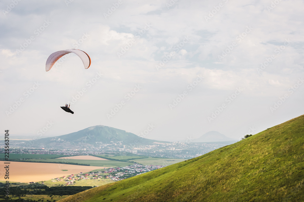 A white-orange paraglider flies over the mountainous terrain A white-orange paraglider flies over the mountainous terrain