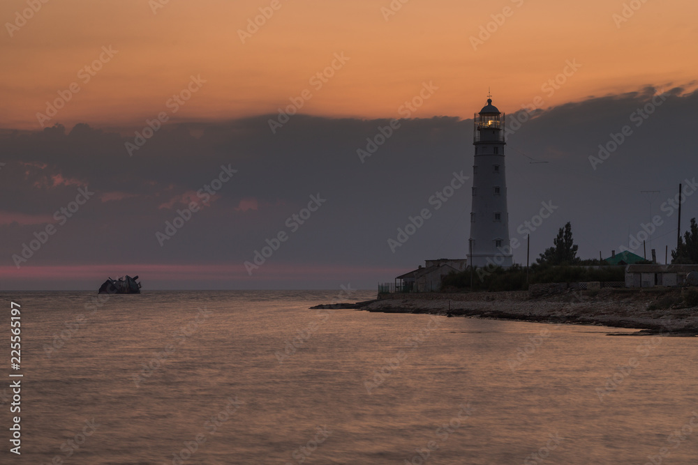 Lighthouse and sunken shipi in sea at sunset