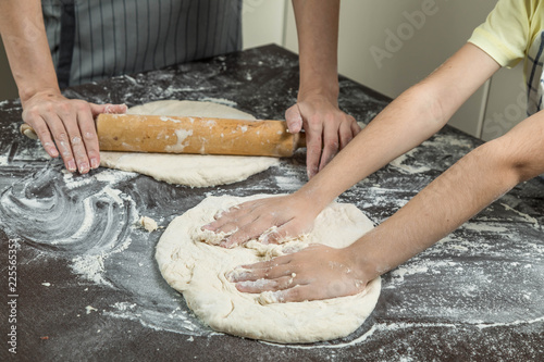 Family cook dough. Hands of the adult and child close up. The child has lifted the rolled dough over a table, and the girl rolls dough with a rolling pin