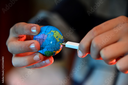Fototapeta Naklejka Na Ścianę i Meble -  A man is trying to charge the planet earth from the network, through a white cable on a red background. The concept of saving the planet.