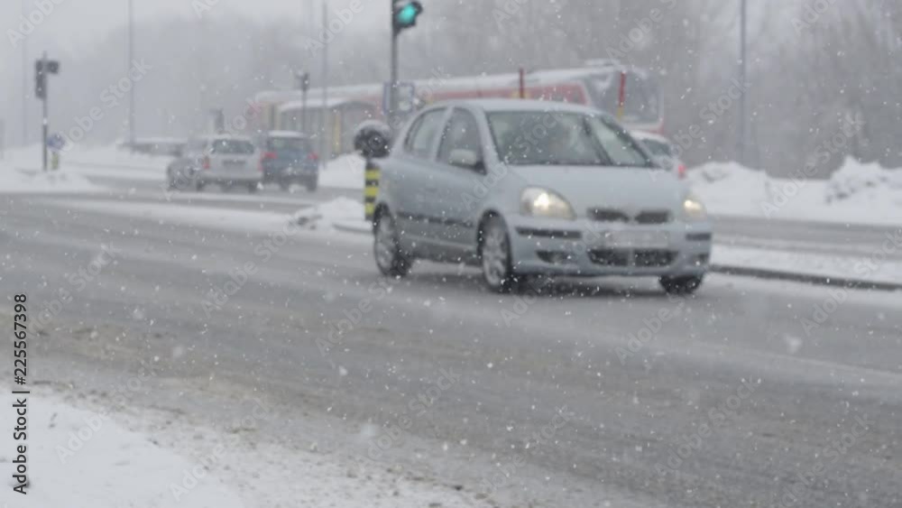 SLOW MOTION, DOF: City traffic driving down the slippery road in the dangerous snowstorm. Cars carefully navigating the slick asphalt streets in the cold winter. Snowy conditions slowing down drivers. SLOW MOTION, DOF: City traffic driving down the slippery road in the dangerous snowstorm. Cars carefully navigating the slick asphalt streets in the cold winter. Snowy conditions slowing down drivers.