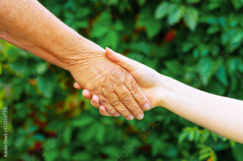 Old and young hold each other's hand, against the blurred background of nature