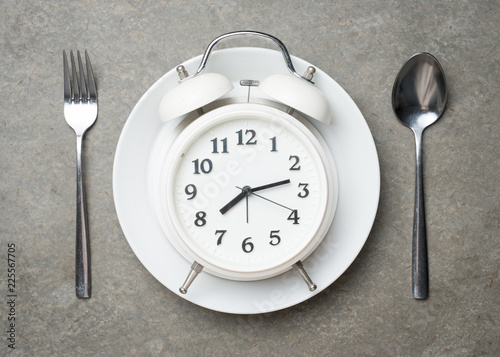 Weight loss or diet concept,Alarm clock on plate with spoon and fork on grey concrete textured