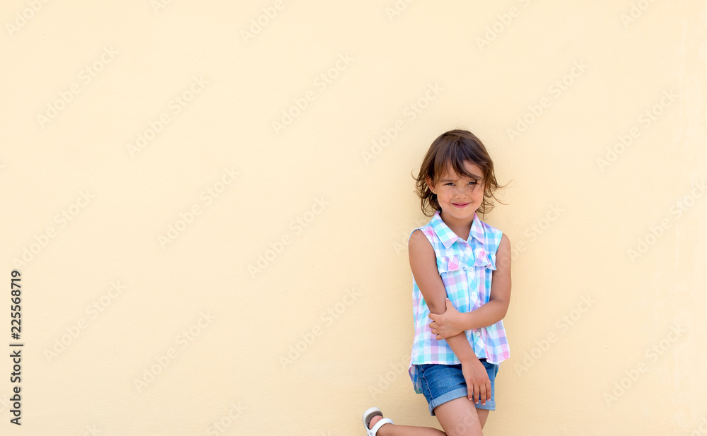 Little girl smiling and possing next to a yellow wall