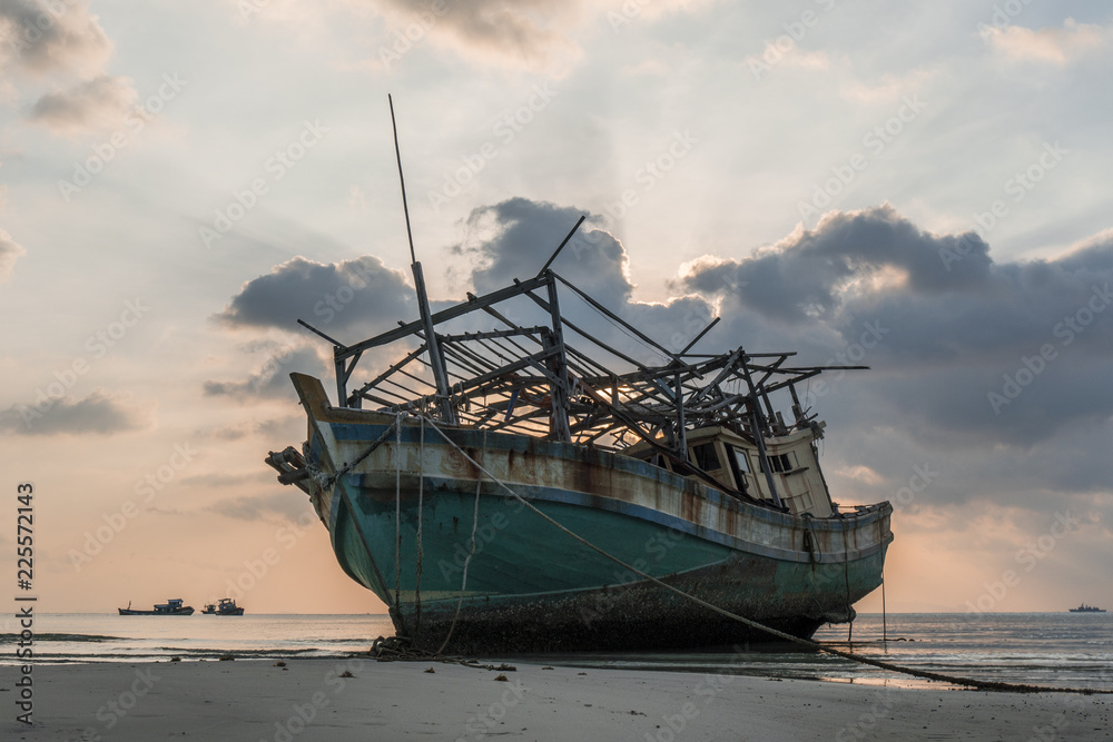 The old wooden ruined fishing boat set aground on the beach at Sunset time The old wooden ruined fishing boat set aground on the beach at Sunset time
