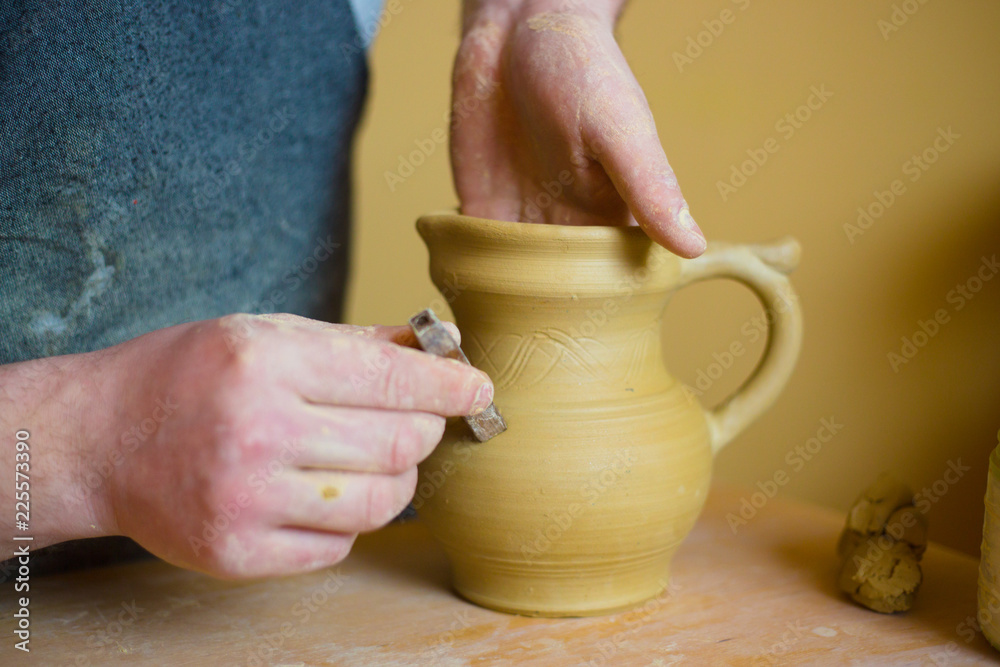 Professional potter making pattern on clay jar with special tool in pottery workshop, studio. Crafting, artwork and handmade concept