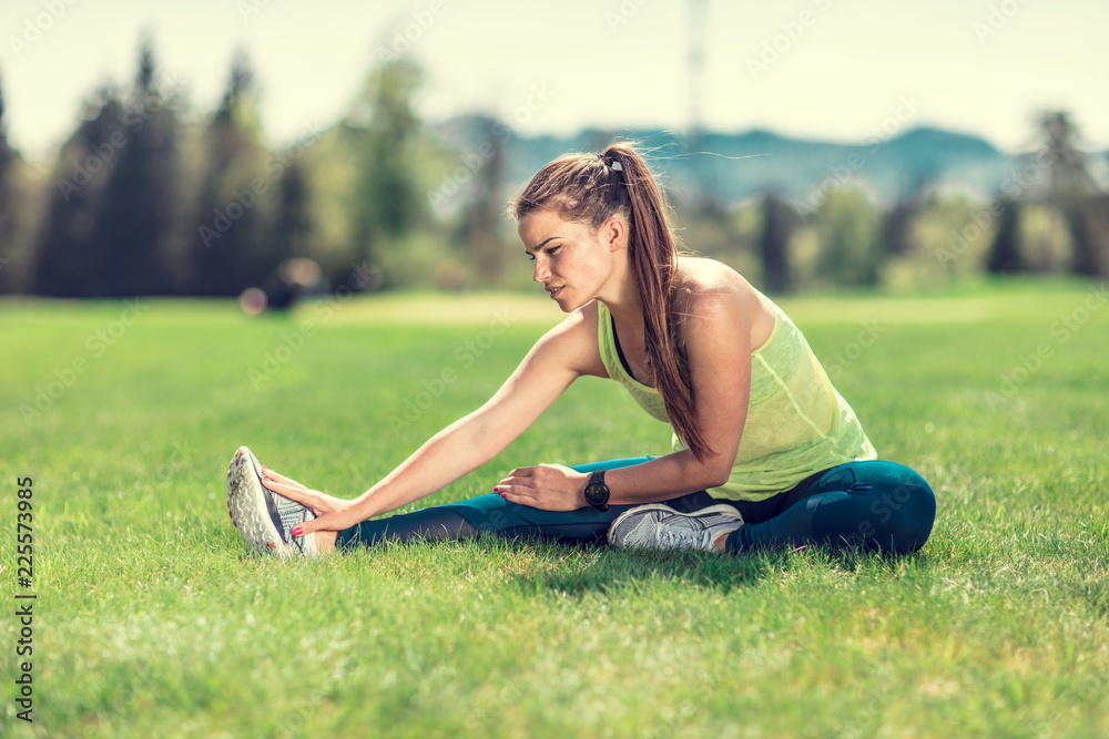 beautiful young sporty brunette relaxing in a park, stretching and looking at her phone beautiful young sporty brunette relaxing in a park, stretching and looking at her phone
