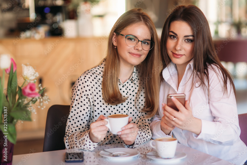 girls sitting in a cafe drinking cappuccino and using telephones