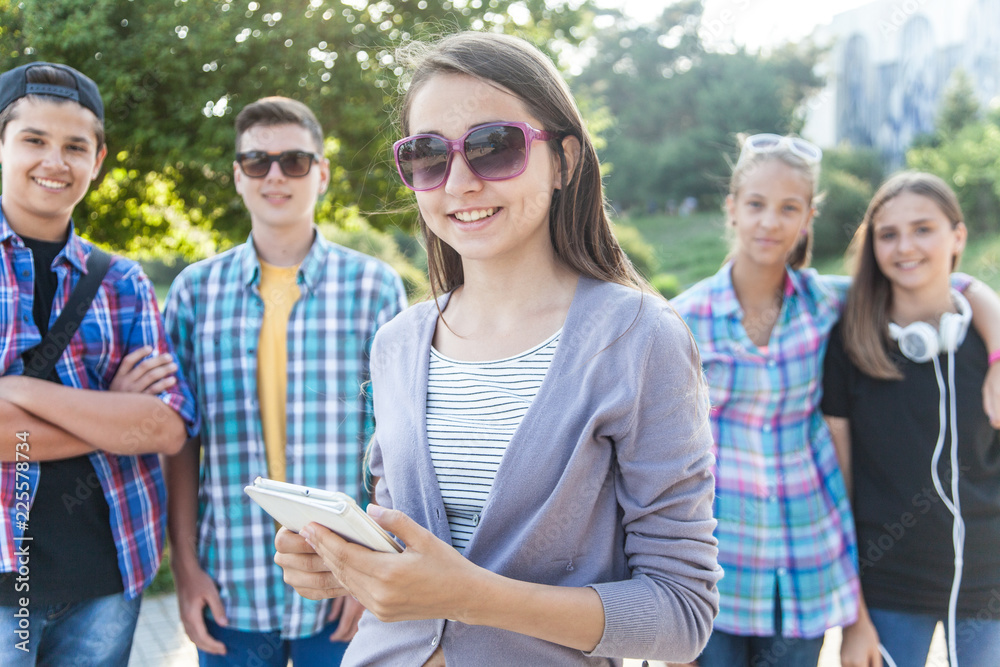 group of teenagers with textbooks and gadgets on background of green park group of teenagers with textbooks and gadgets on background of green park