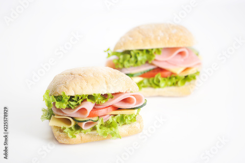 Two sandwiches on a white background. At the heart of the mini ciabatta sandwich. A filling of slices of ham, cheese, lettuce, fresh cucumbers and tomatoes. Close-up.