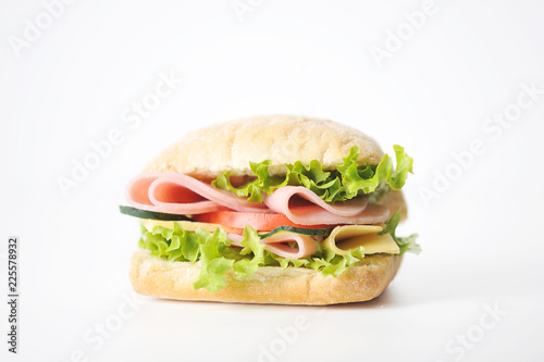 Sandwich on a white background. At the heart of the mini ciabatta sandwich. A filling of slices of ham, cheese, lettuce, fresh cucumbers and tomatoes. Close-up.