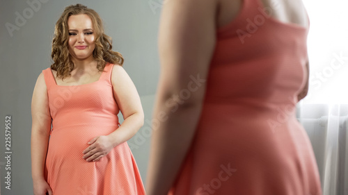 Overweight lady unhappy with her mirror reflection, afterbirth stage depression photo