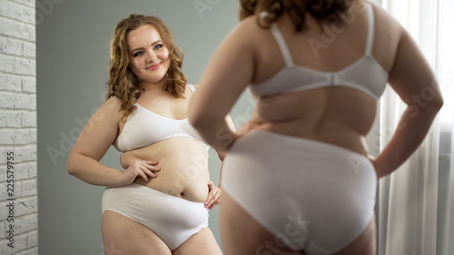 Happy fat female looking at her reflection, admiring feminine plump body photo