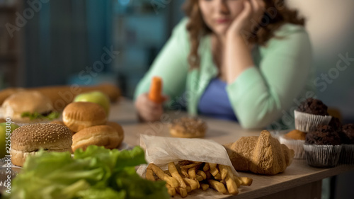 Depressed fat lady sitting at table full of unhealthy junk food, overeating photo