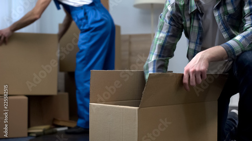 Man unboxing things in new apartment, moving company worker bringing boxes