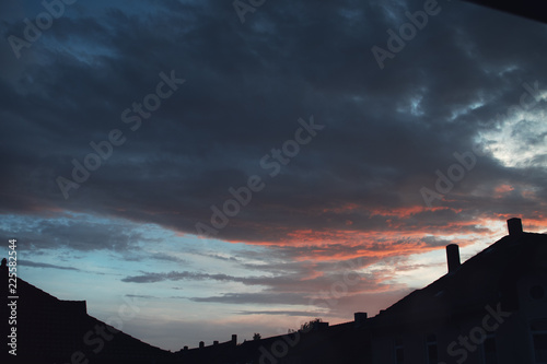 Urban house roof silhouettes at dramatic colorful sunset sky with red clouds and blue night twilight sky.