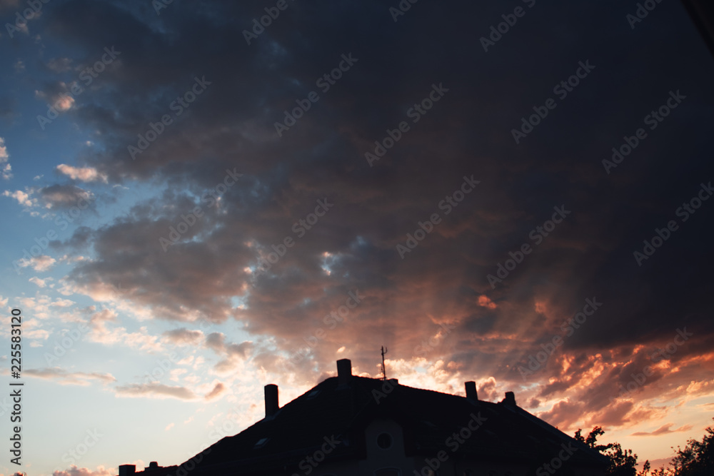 Cityscape with roof tops silhouettes and dramatic epic colorful orange burning clouds and blue sky with small textured clouds. Braunschweig, Germany