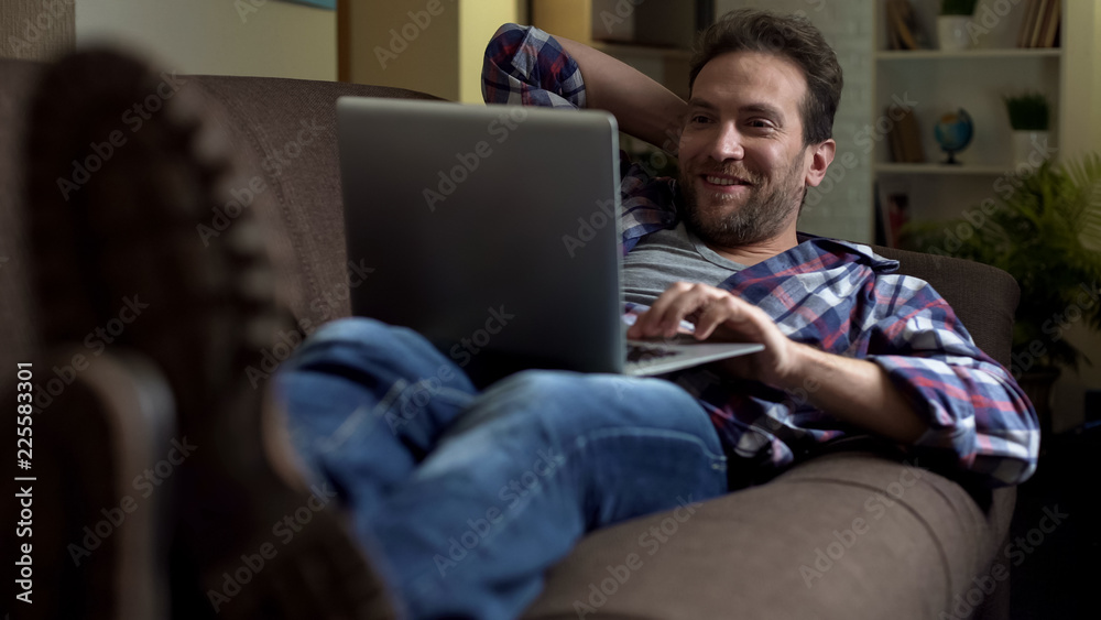Man lying on couch with laptop, getting surprised at exciting news on screen