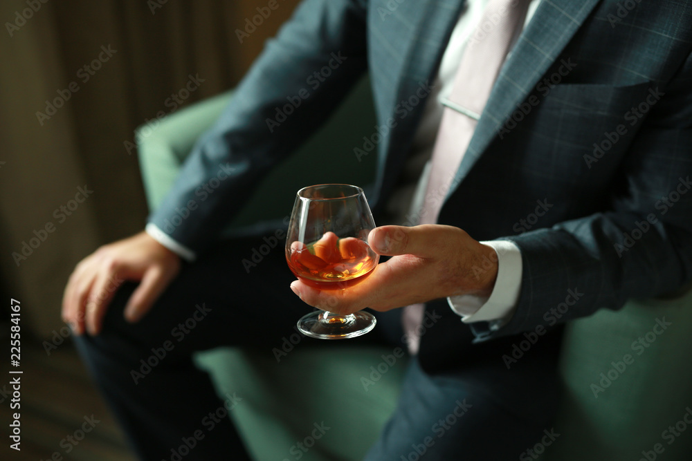 man sitting in a chair in a stylish suit with a glass of alcohol in his hand